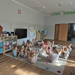 dzieci siedzą na dywanie z uniesionymi kończynami