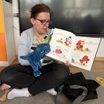 pani trzyma książkę i maskotkę dinozaura